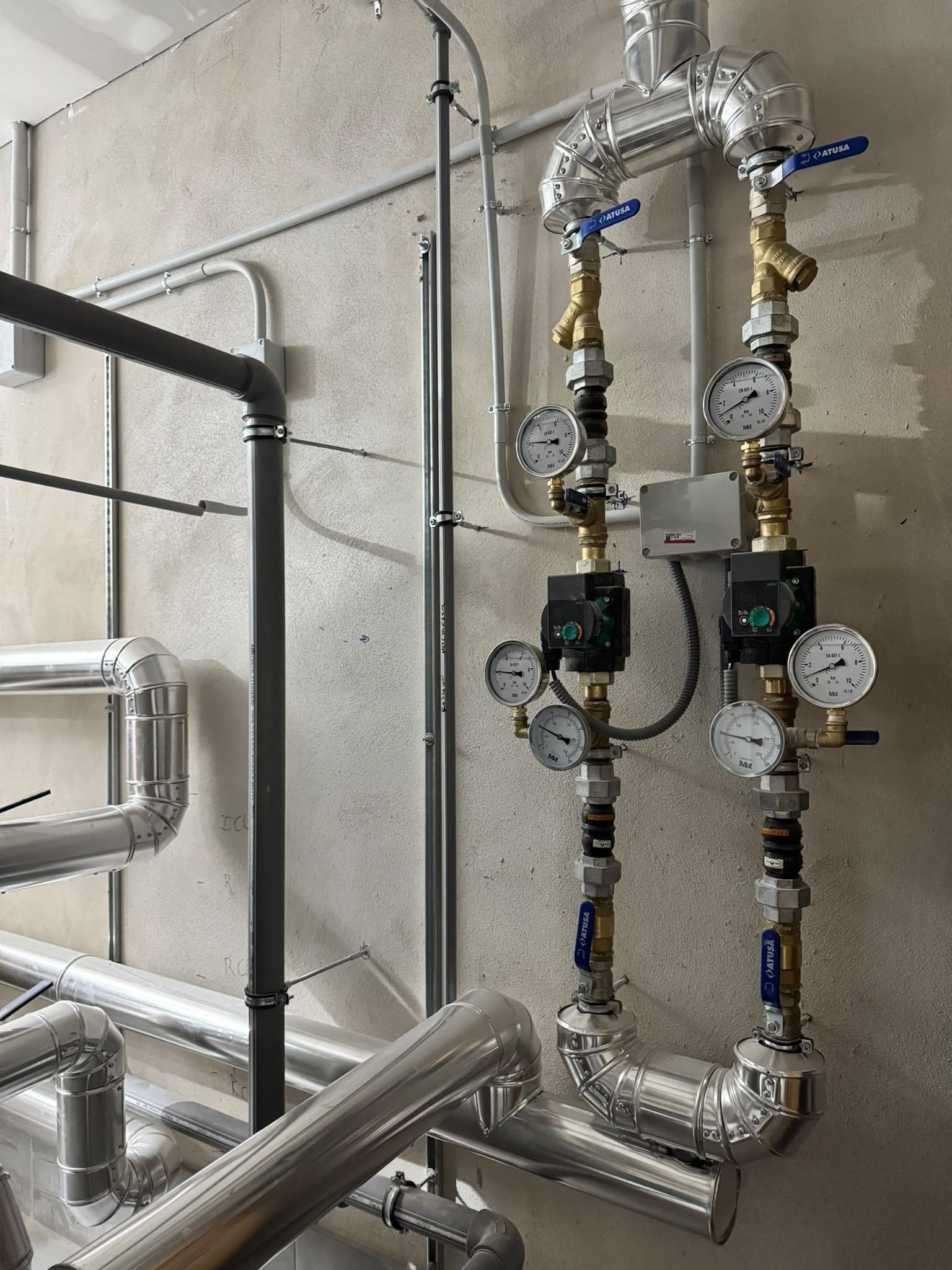 Tuberías industriales y manómetros en una pared, con tuberías metálicas aisladas y válvulas en una sala de máquinas