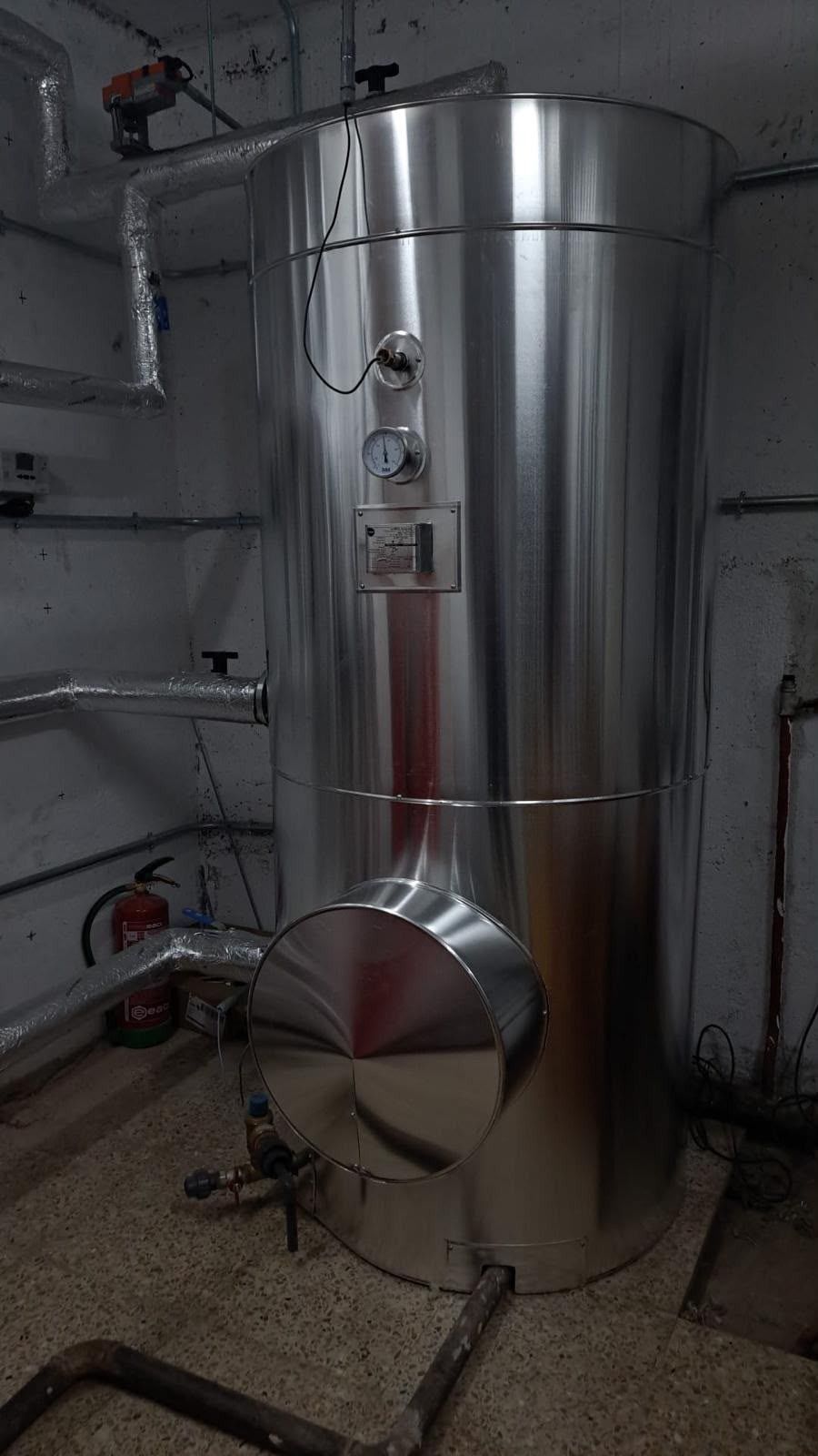Gran depósito industrial de acero inoxidable con tuberías y medidores en una sala de instalaciones