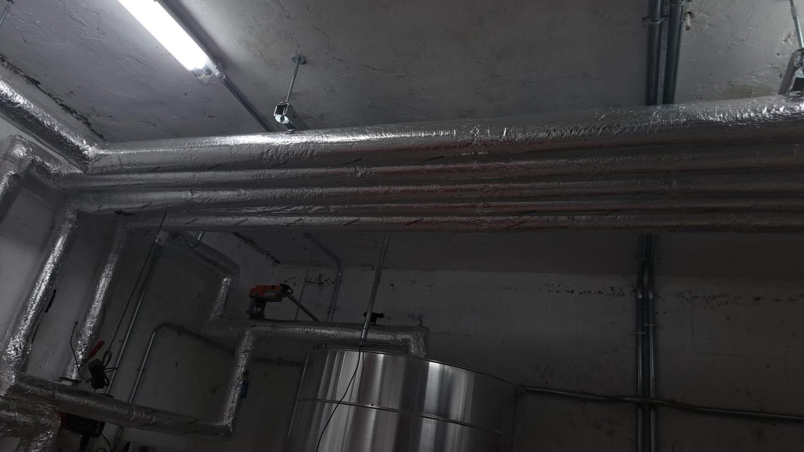 Conductos metálicos y tuberías aisladas en el techo de una sala industrial