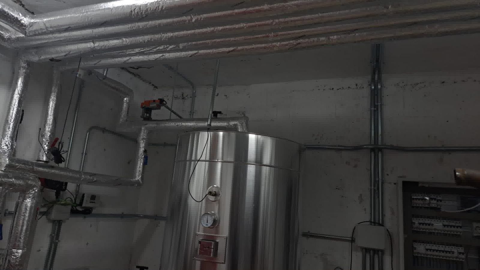 Sótano industrial con conductos plateados, tuberías y grandes depósitos metálicos en una sala de instalaciones