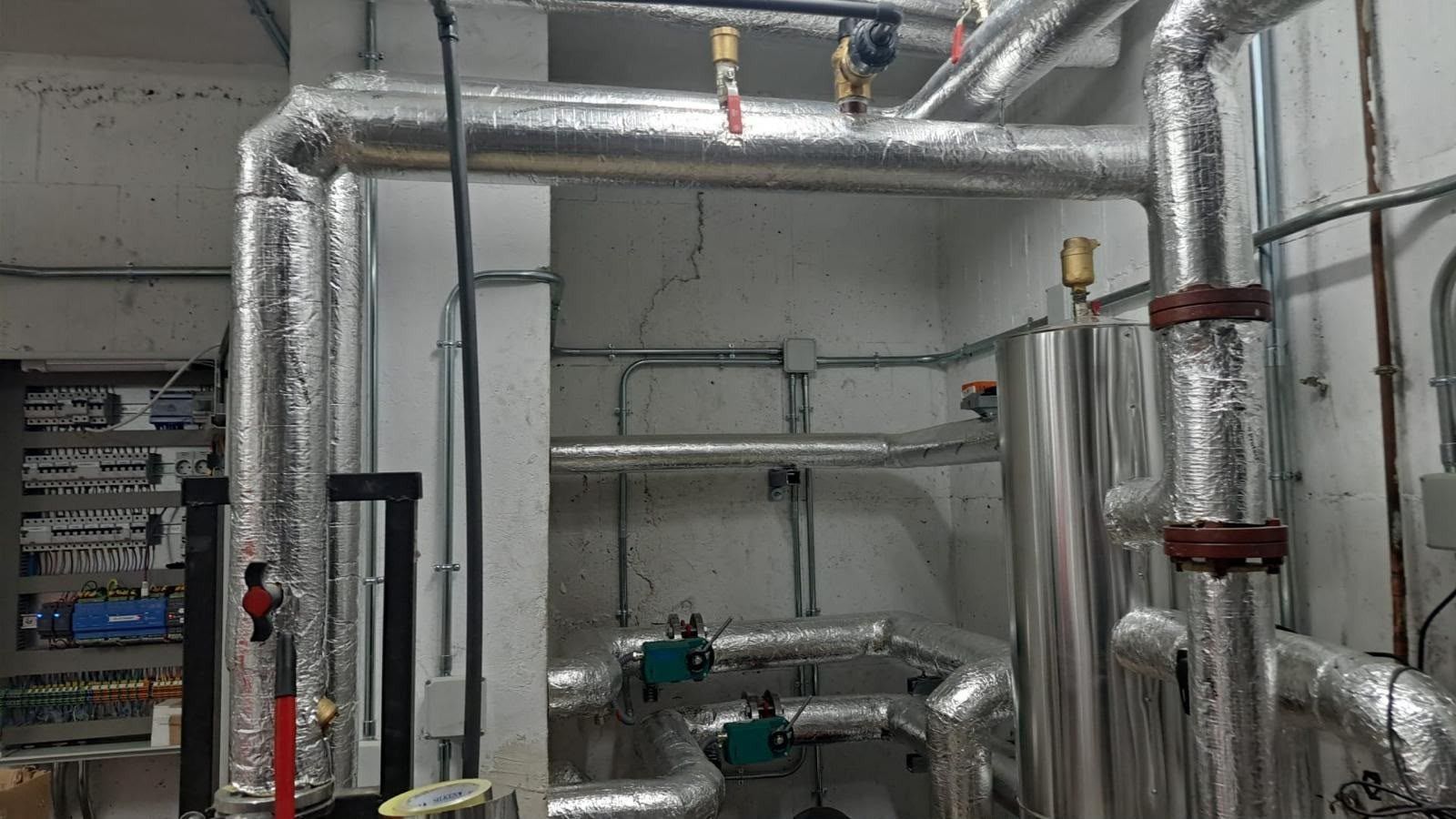 Tuberías y conductos metálicos en una sala de servicios industriales, con tuberías plateadas aisladas y válvulas