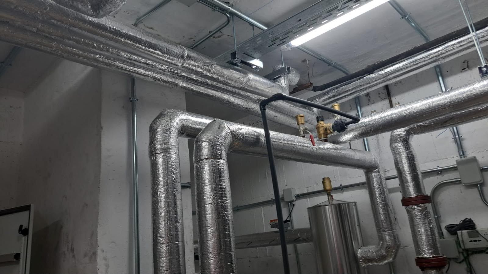 Techo industrial con tuberías, conductos y válvulas aislados de color plateado en una sala de máquinas