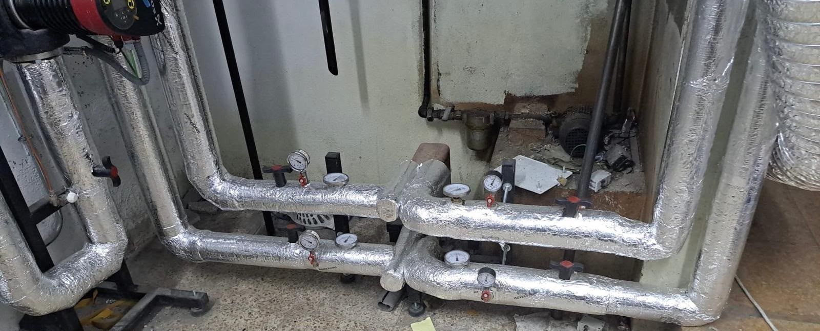 Conductos y tuberías de climatización envueltos en papel de aluminio a lo largo de una pared del sótano