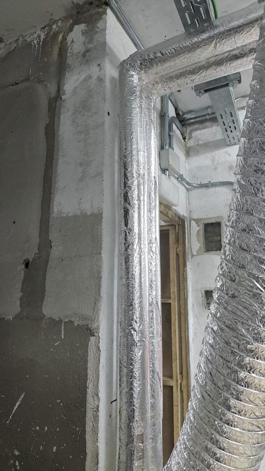 Obra en construcción con paredes grises sin terminar y una puerta cubierta con plástico protector.