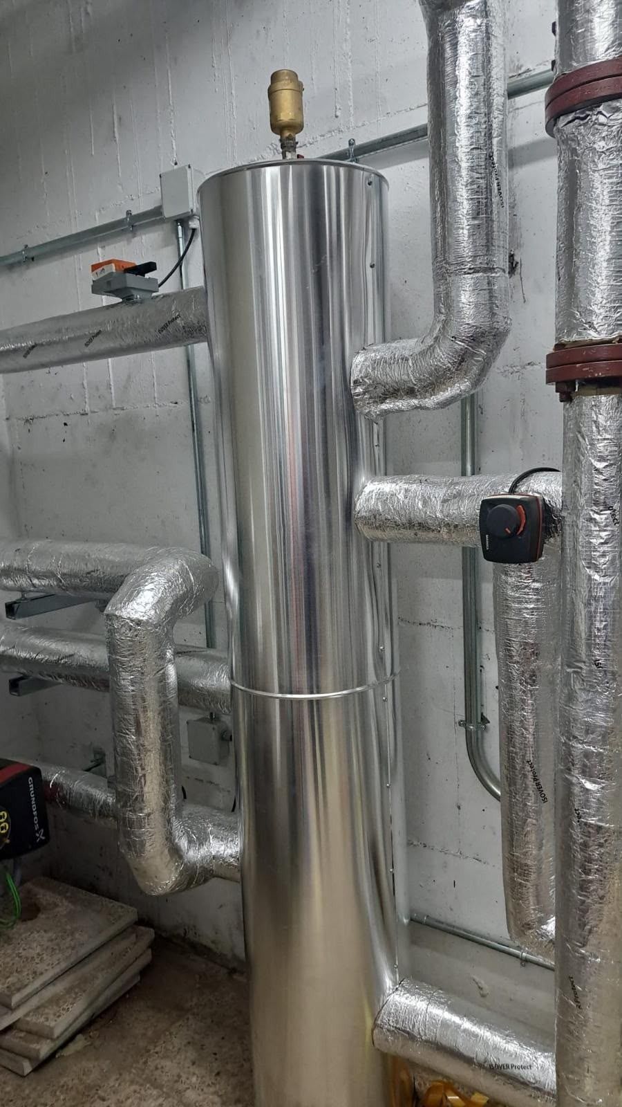 Tanque metálico brillante con tuberías aisladas en una sala de servicios industriales