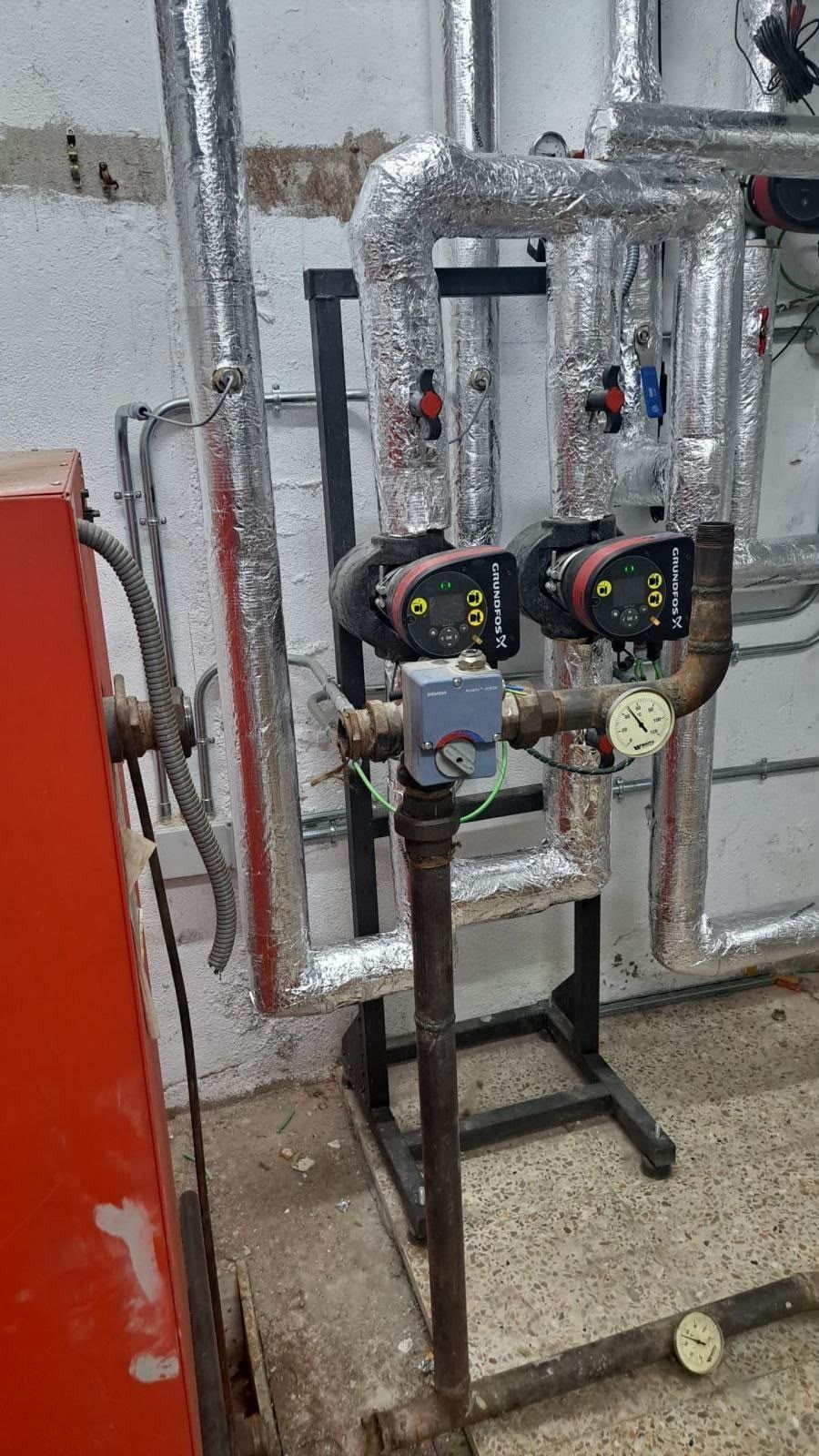 Tuberías industriales y dos bombas negras montadas sobre soportes metálicos en una sala de instalaciones