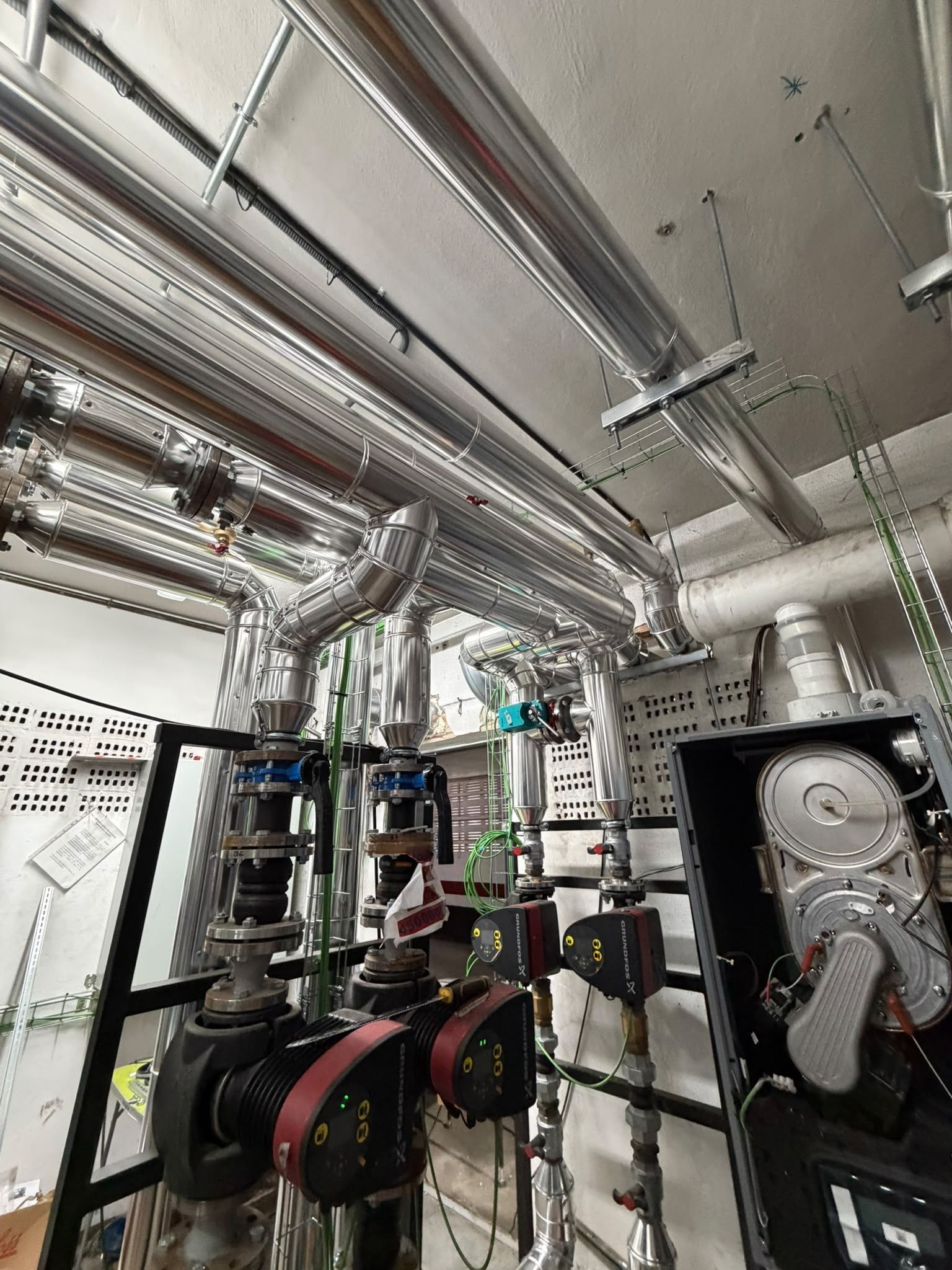 Sala de maquinaria industrial con tuberías y bombas de metal pulido bajo un techo blanco y bajo