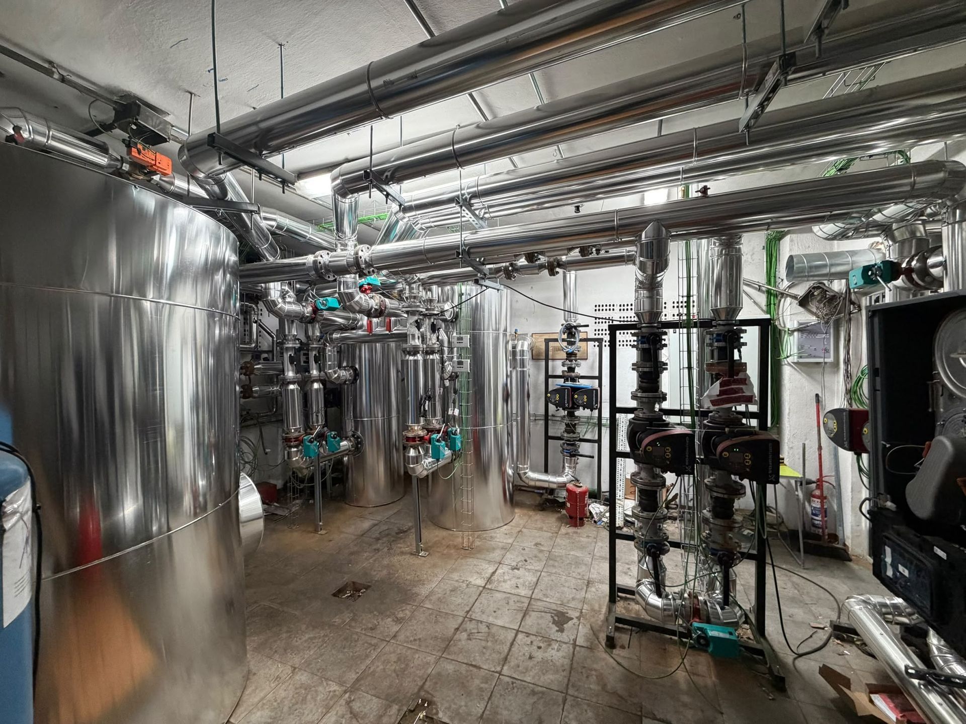 Sala de una planta industrial con depósitos, tuberías y válvulas de acero inoxidable bajo una intensa iluminación cenital