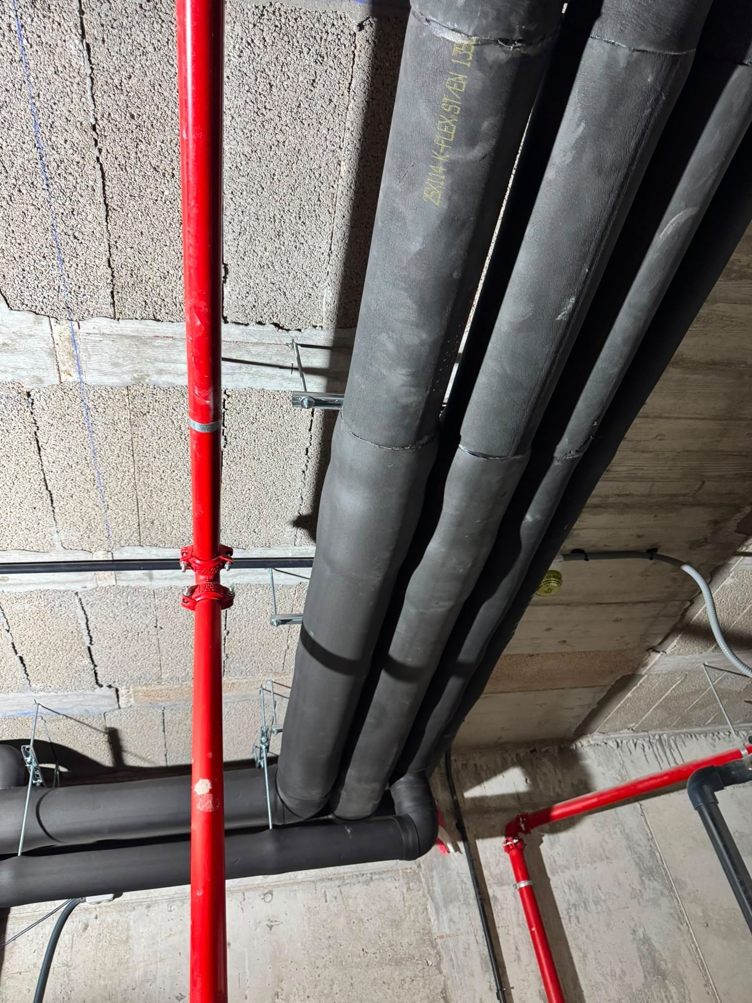 Tuberías de servicio rojas y negras que recorren el techo de hormigón de un espacio técnico sin terminar