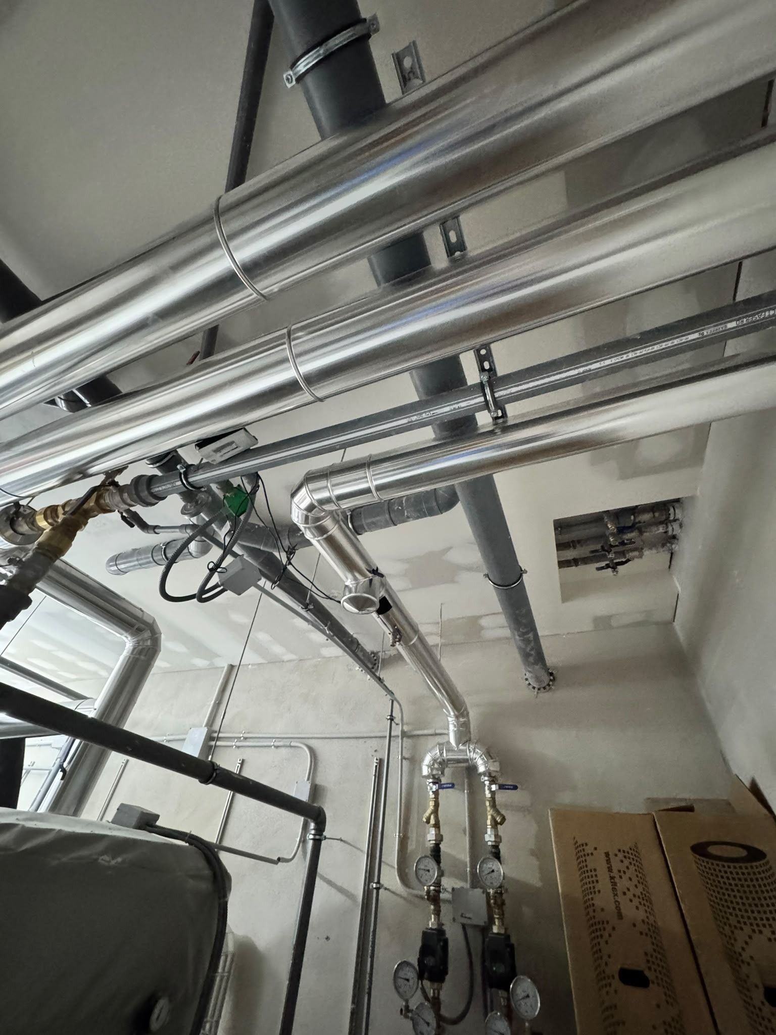 Techo industrial con tuberías, cables y conductos plateados en una sala de instalaciones.