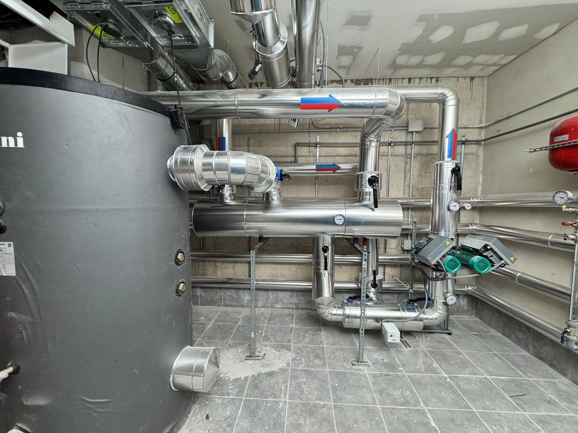 Sala de calderas industrial con tuberías metálicas, válvulas y tanques sobre un suelo de baldosas