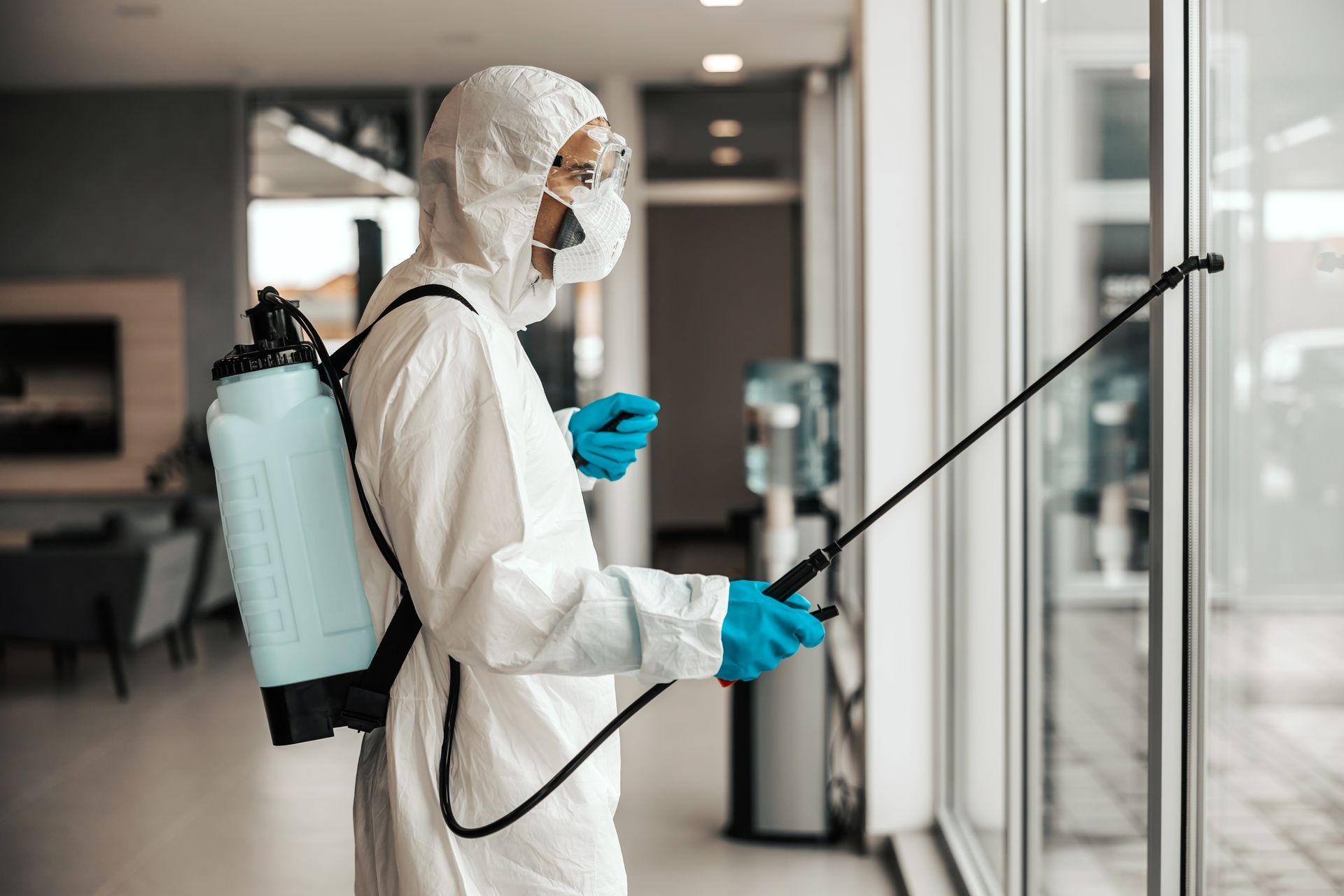 Professionnel en tenue blanche qui pulvérise du produit dans un hall d’entreprise
