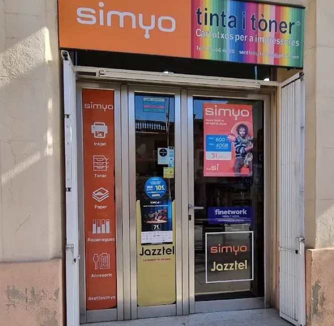 Fachada de la tienda de móviles y tinta/tóner Simyo, con puertas de cristal y letreros coloridos.