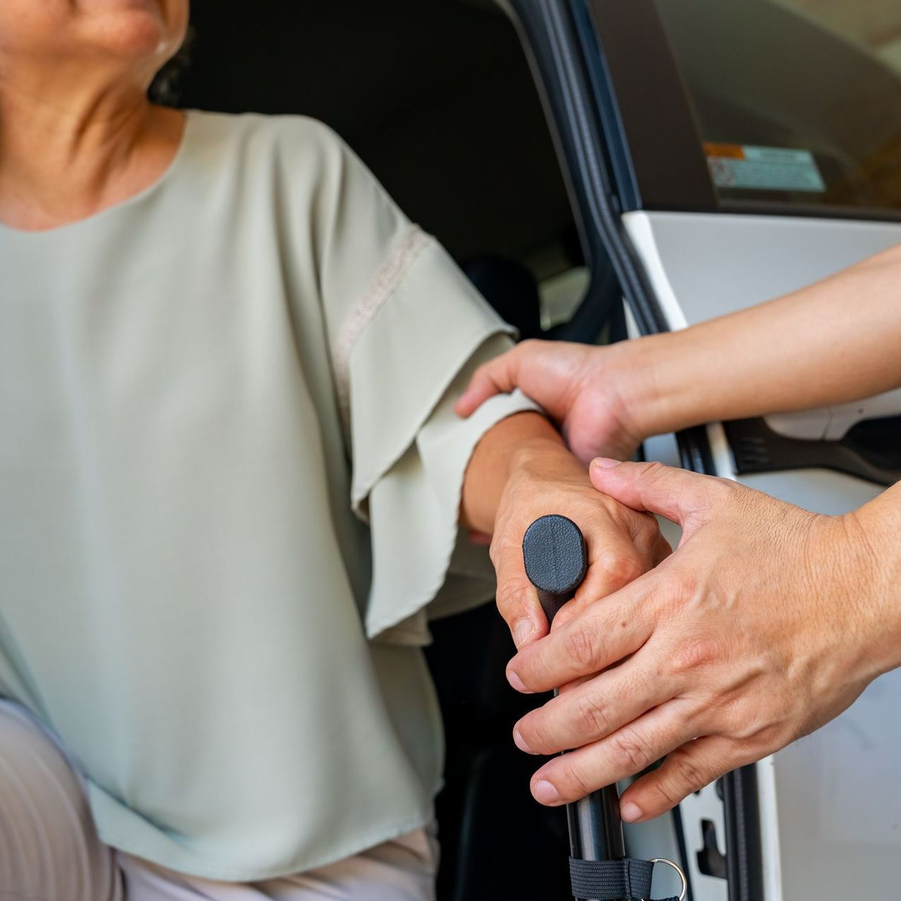 Personne aidant une femme munie d'une canne à sortir de la voiture