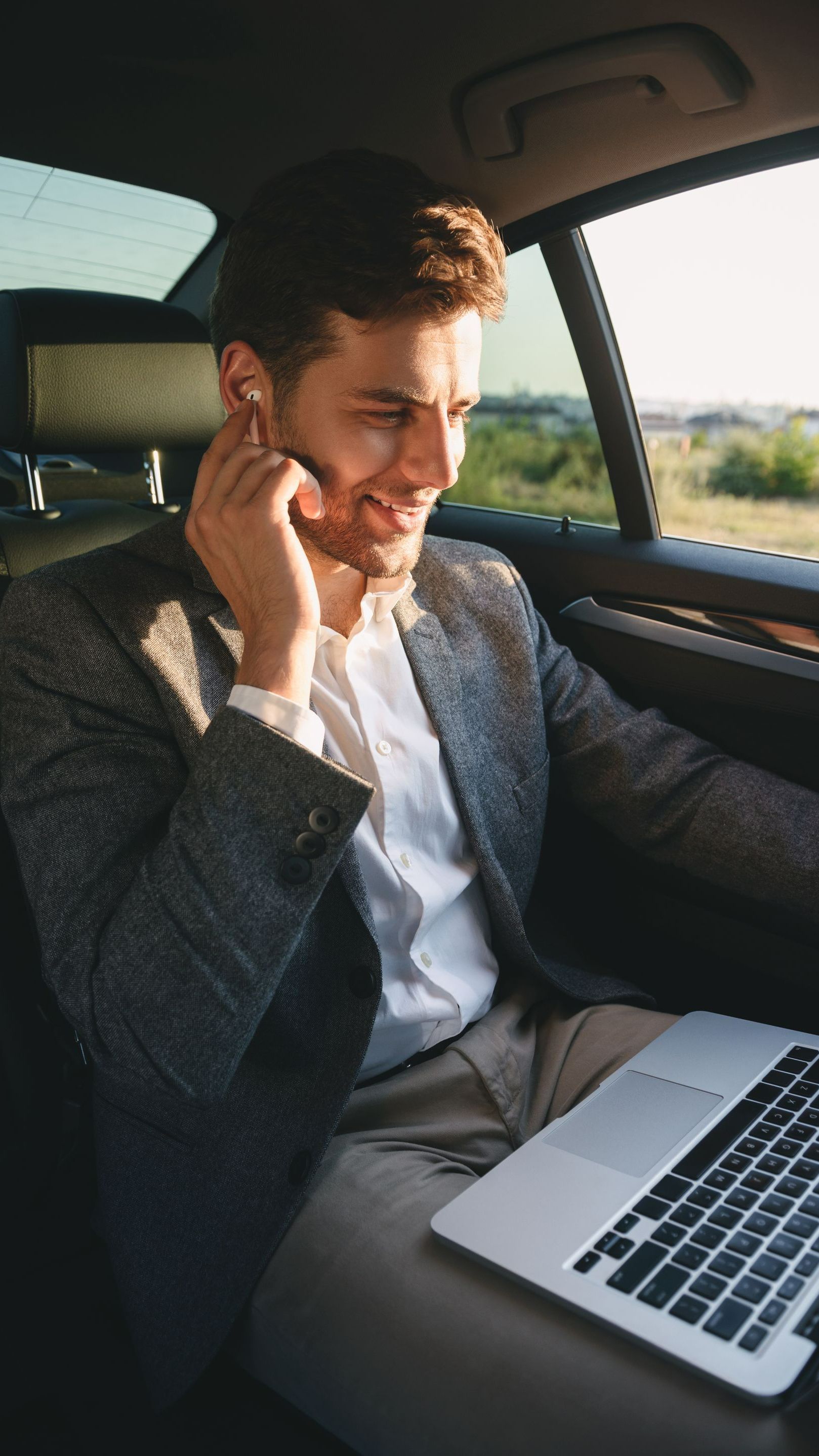 Un homme avec un airpod et un ordinateur sur ses genoux à l'arrière d'une voiture