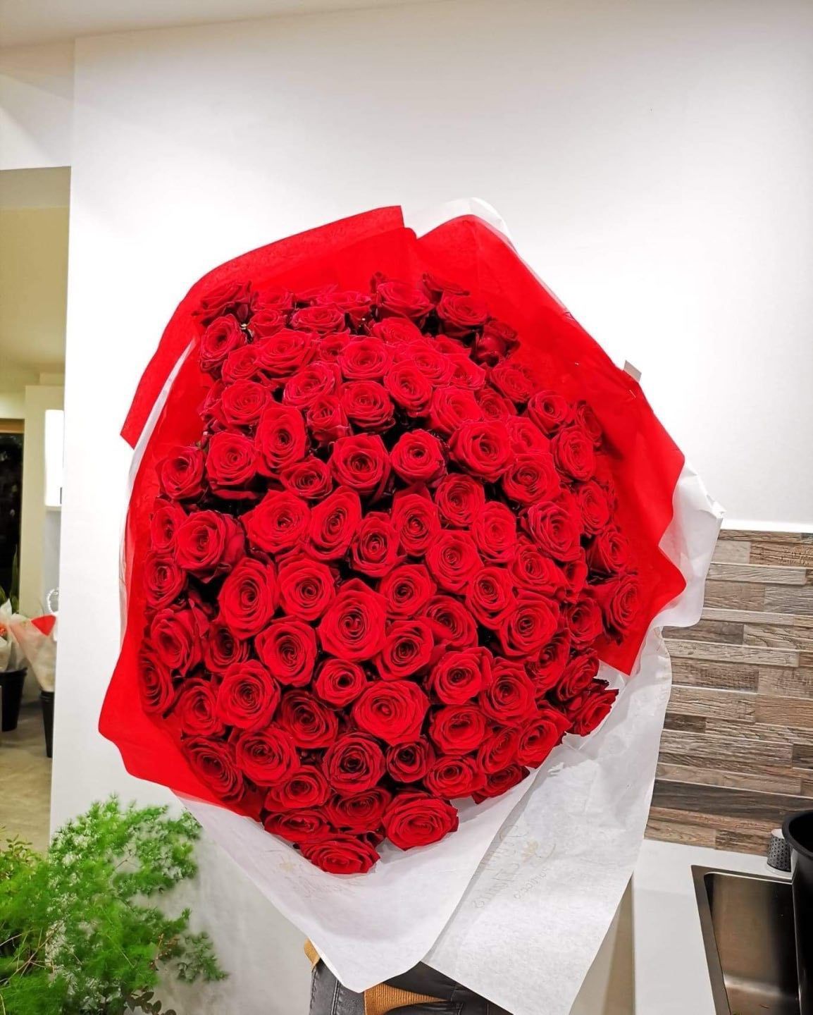 Gros bouquet de roses rouges emballé dans du papier rouge et blanc.