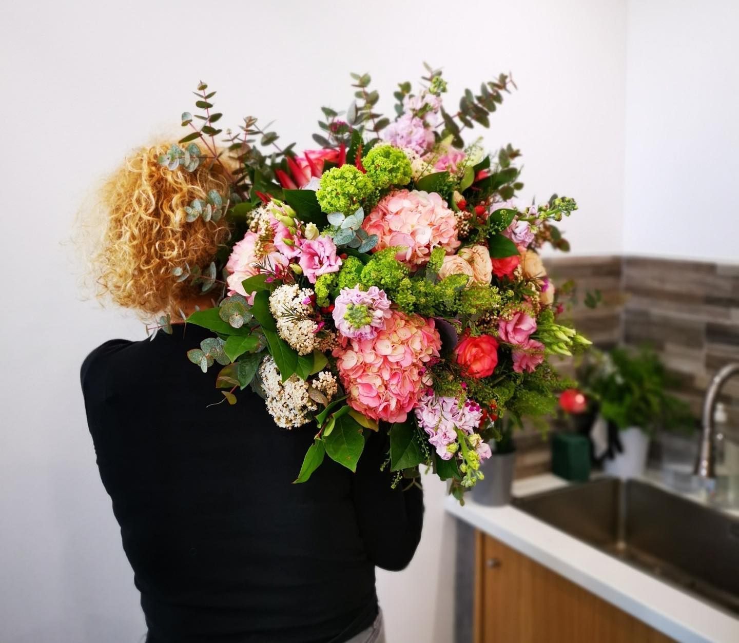 Une femme tenant un grand bouquet de fleurs roses, vertes et rouges près d'un évier.