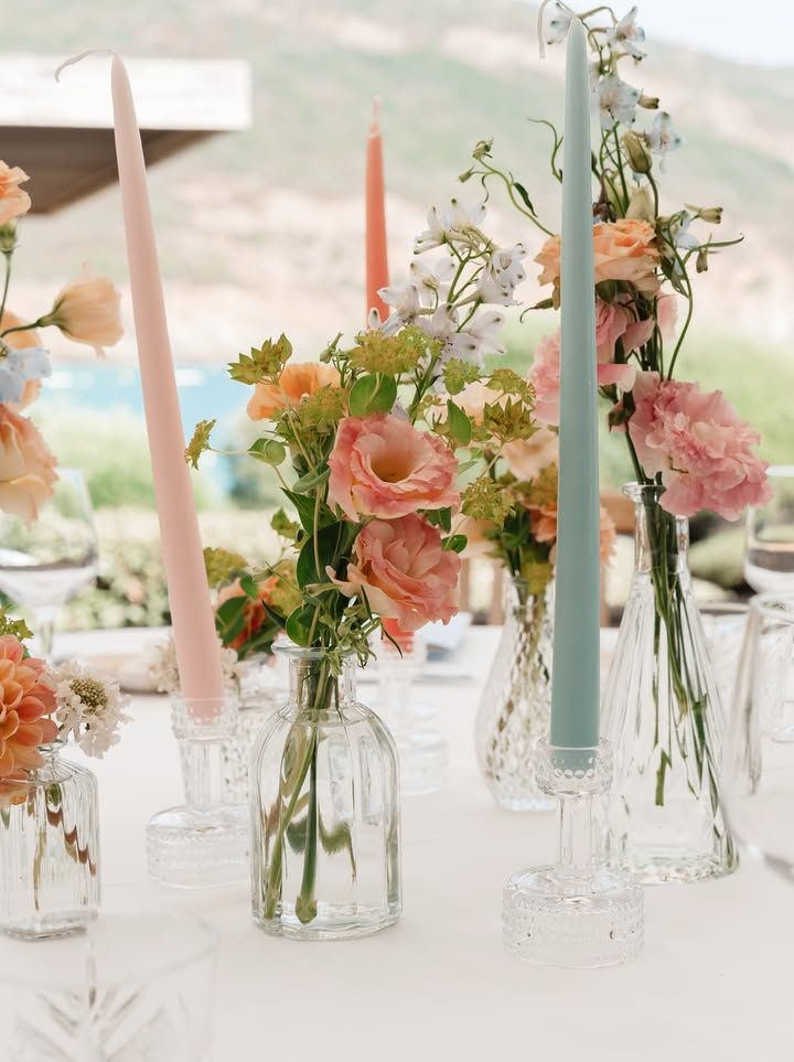 Table dressée avec des fleurs, des bougies et des vases en verre. Les couleurs pastel créent une ambiance élégante.