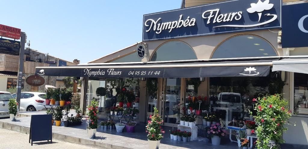 Extérieur de Nymphéa Fleurs, une boutique de fleurs, avec un auvent noir et diverses compositions florales exposées.