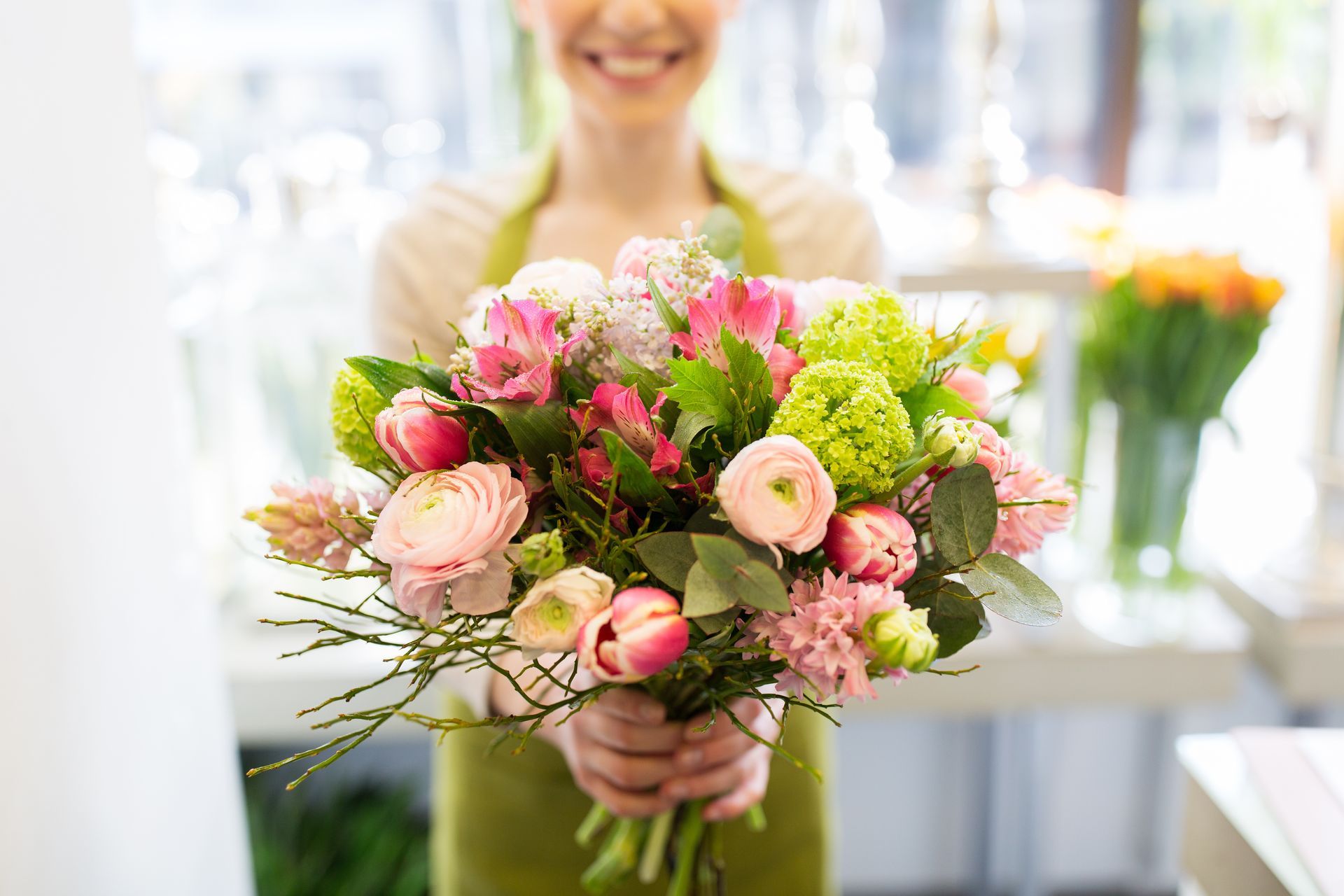 Femme en tablier souriante, tenant un bouquet de fleurs roses et vertes.