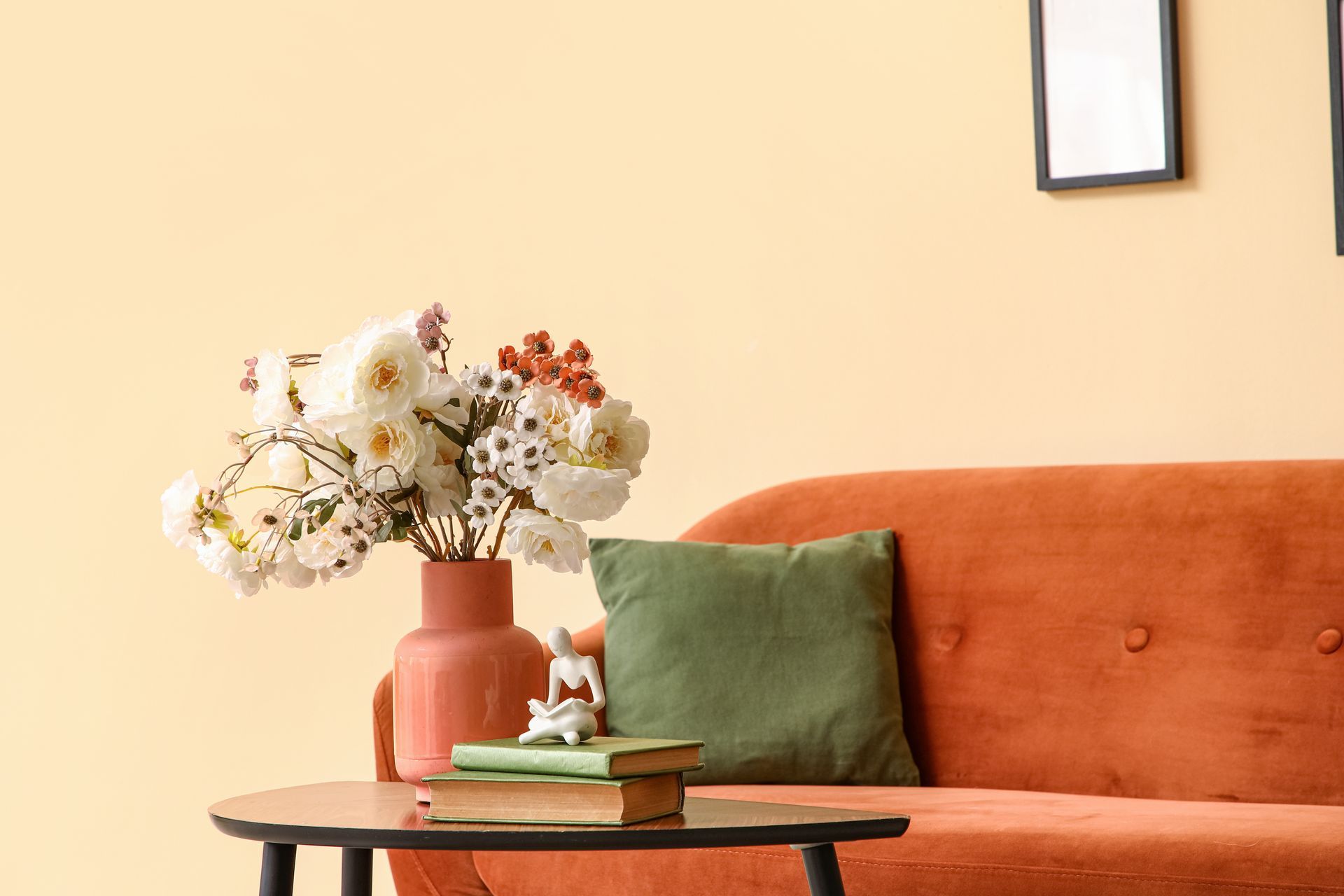 Canapé orange avec coussin vert, table basse avec livres et fleurs, mur beige.