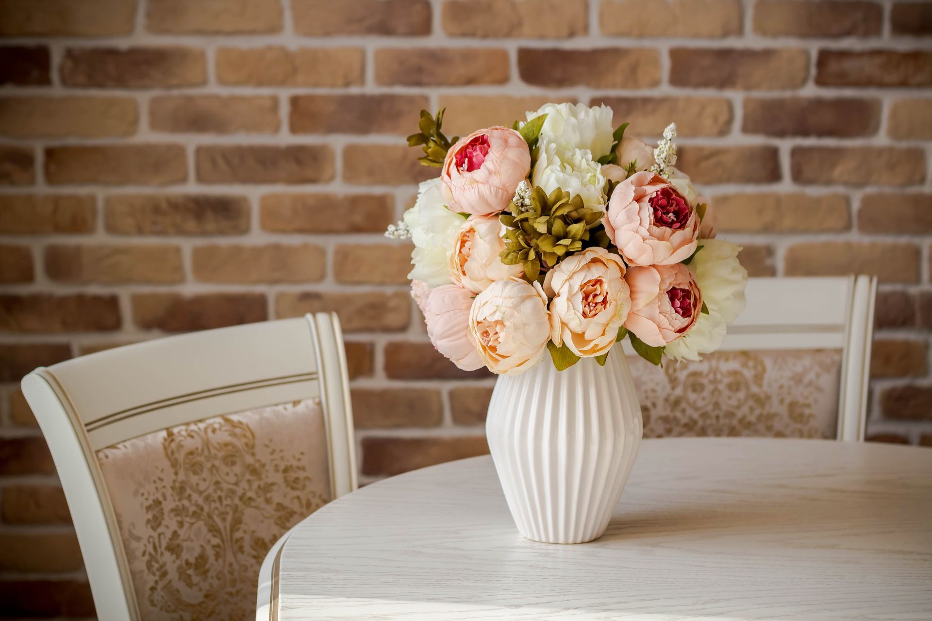 Vase blanc contenant des fleurs roses et blanches sur une table blanche, mur de briques en arrière-plan.