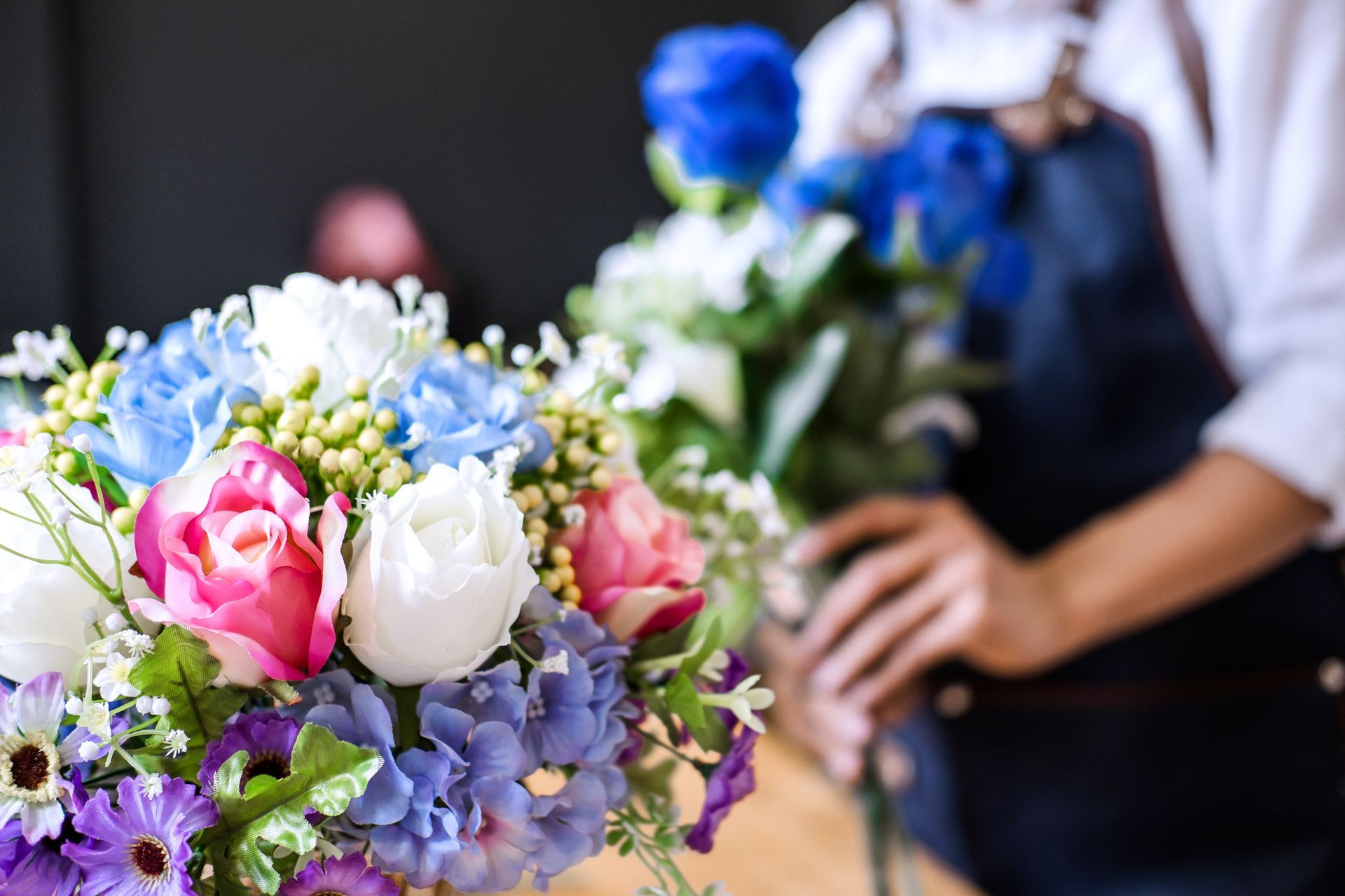 Une fleuriste compose un bouquet de fleurs colorées, notamment des roses bleues, roses et blanches.