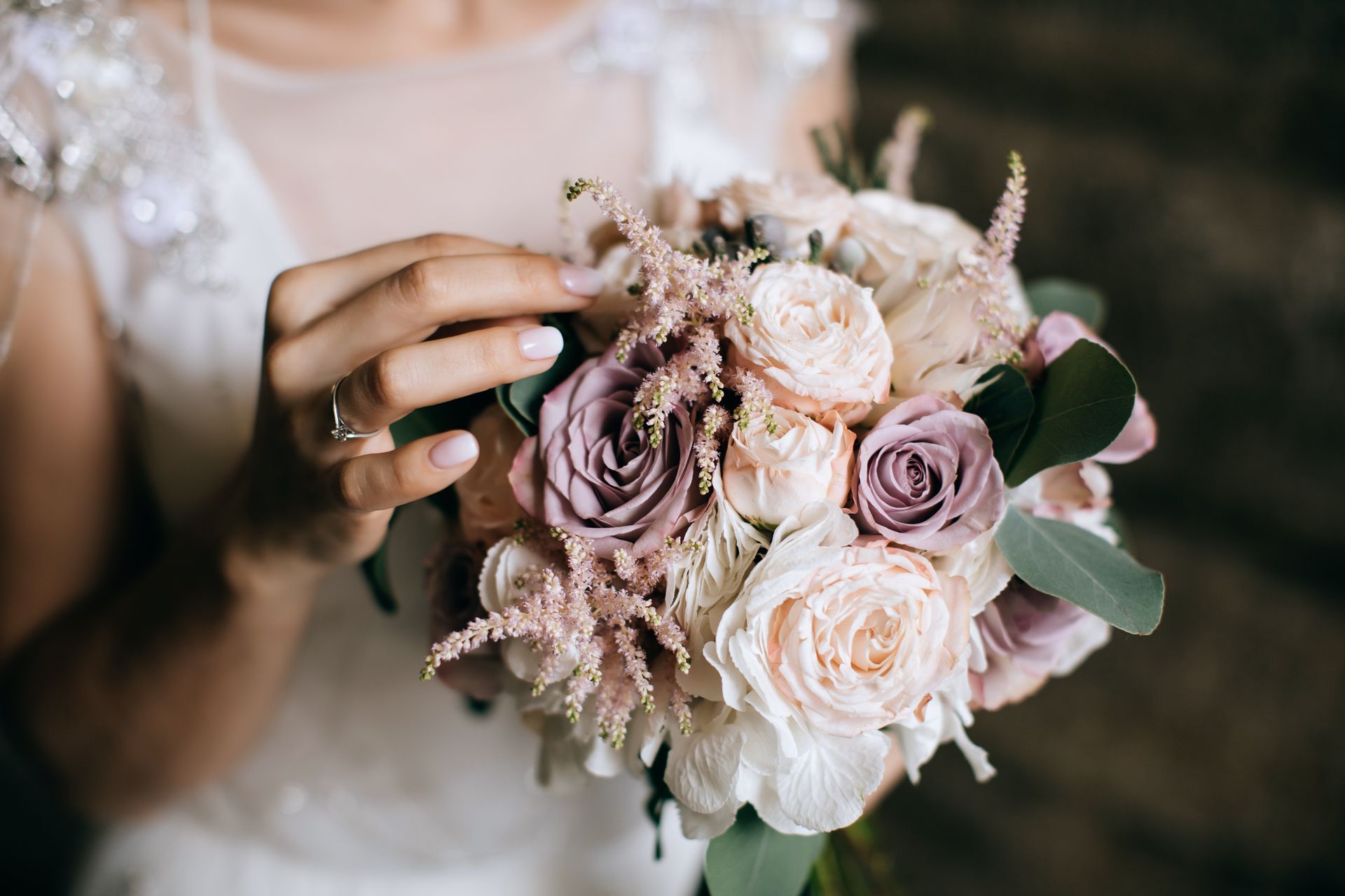 La mariée tient un bouquet de roses roses, lavande et blanches et porte une robe de mariée blanche.