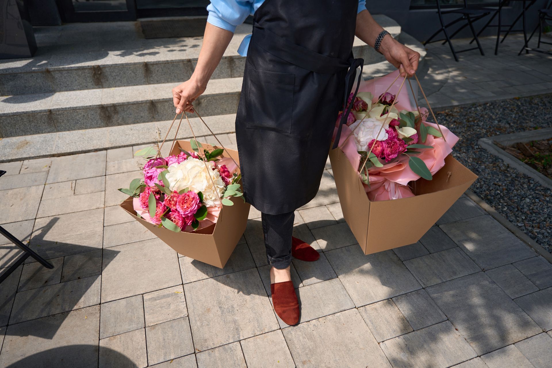 Une personne transporte à l'extérieur deux boîtes en carton remplies de bouquets de fleurs colorés.