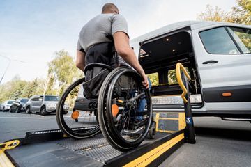 Person im Rollstuhl wird mit einer Rampe in ein Taxi gebracht