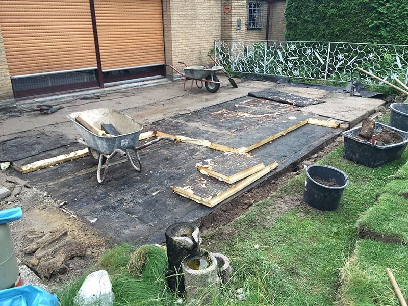 Vor einer Garage steht eine Schubkarre auf dem Boden.