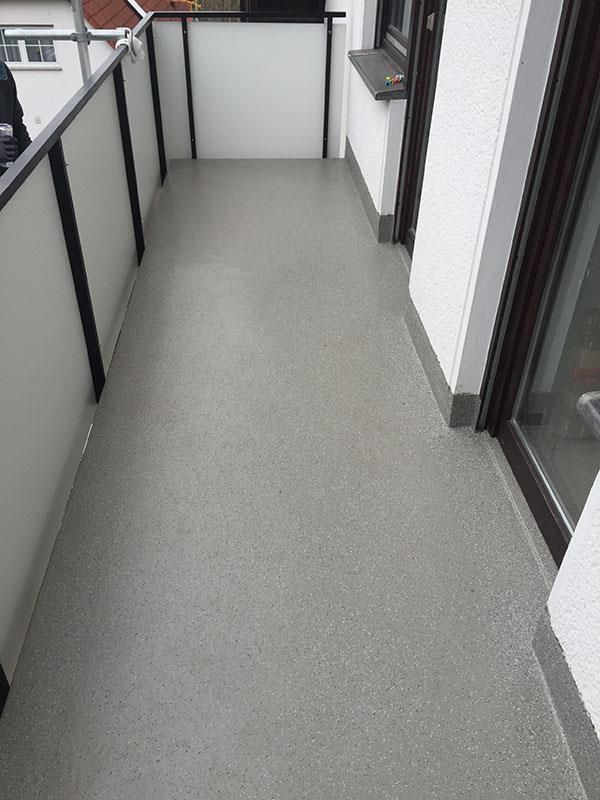 Ein Balkon mit grauem Boden und weißem Geländer.