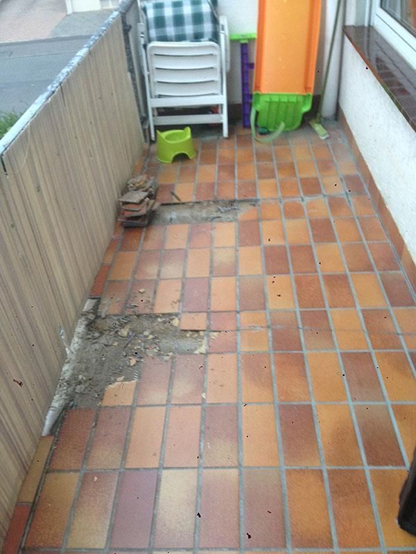 Ein Balkon mit kaputtem Fliesenboden und einem Stuhl