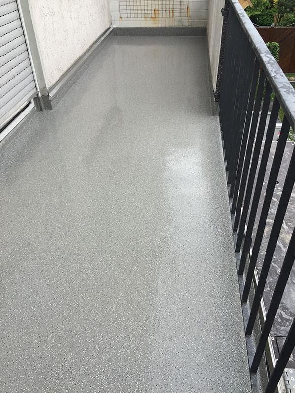 Ein Balkon mit schwarzem Geländer und grauem Boden.