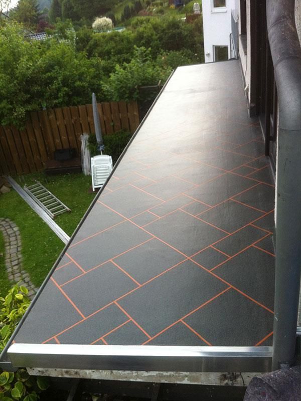 Ein Balkon mit gefliestem Boden und einem Zaun im Hintergrund.