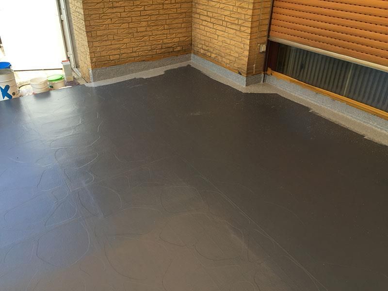 In einem Raum mit einer Ziegelwand wird ein grauer Boden gestrichen.