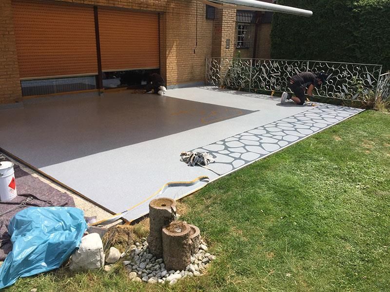 Ein Mann streicht eine Einfahrt vor einem Haus.