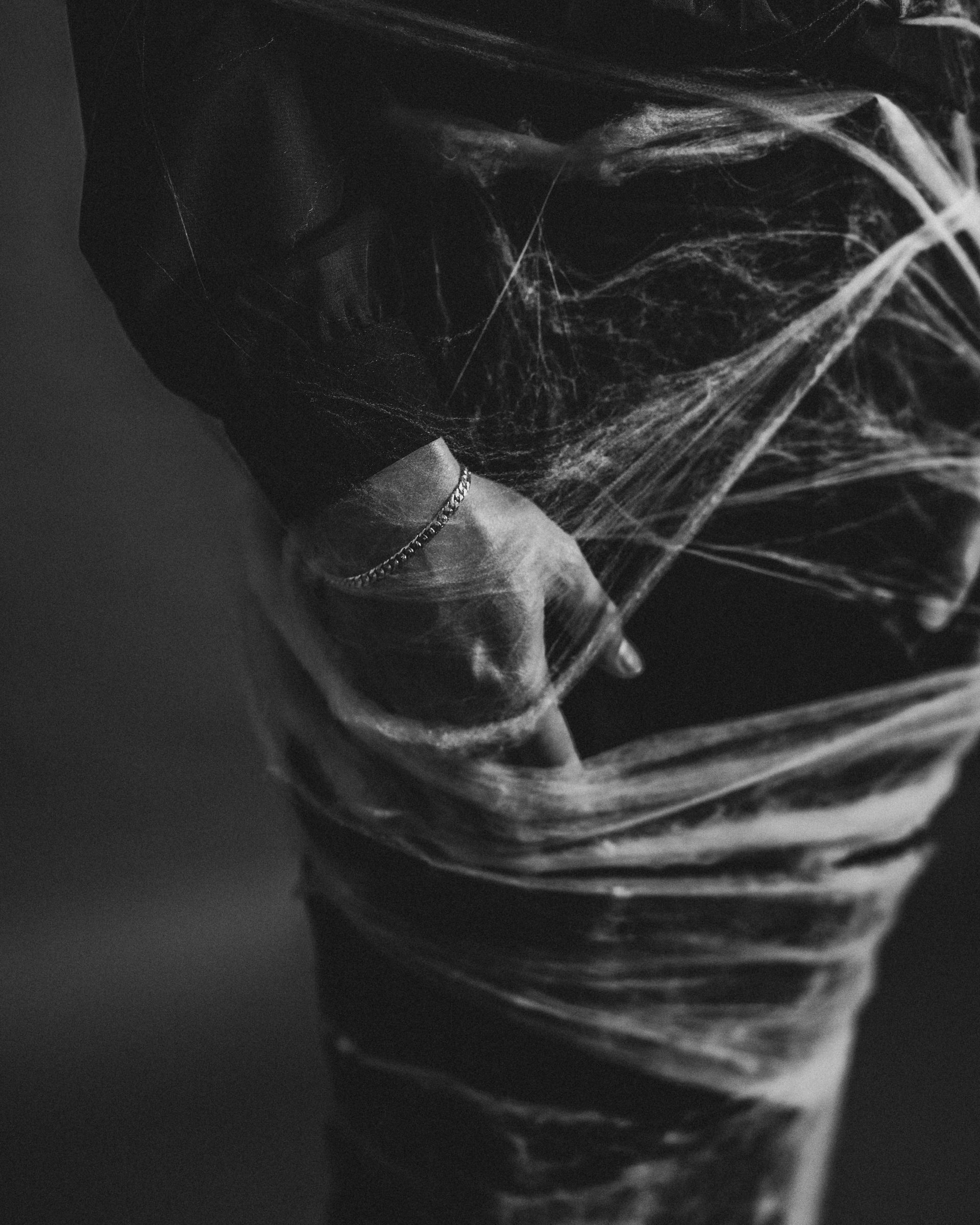 El brazo y el torso de una persona están envueltos en material translúcido. Una mano con un brazalete reposa sobre el cuerpo envuelto.