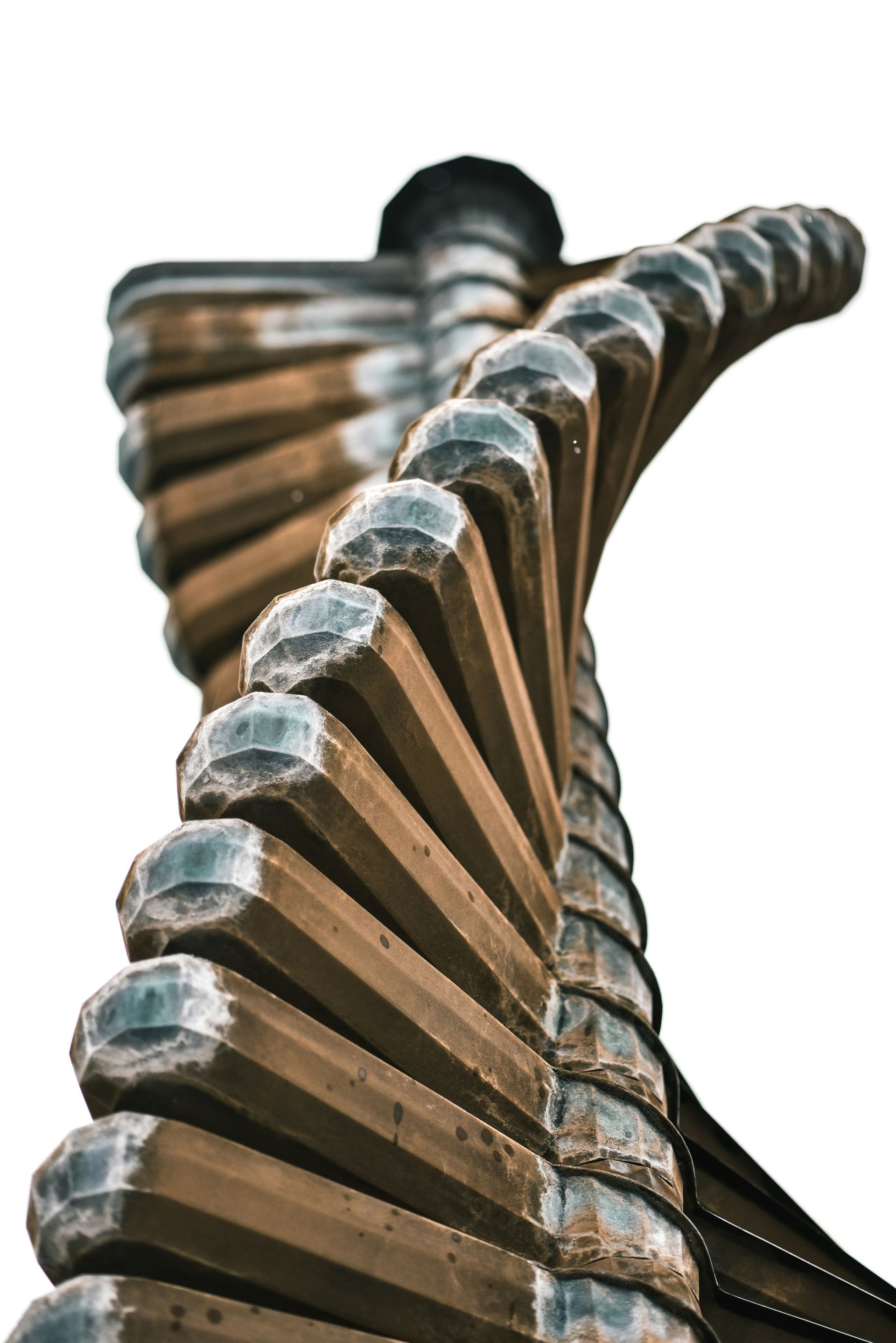 Escultura de metal retorcido, de color marrón y plateado, que asciende en espiral sobre un fondo blanco.