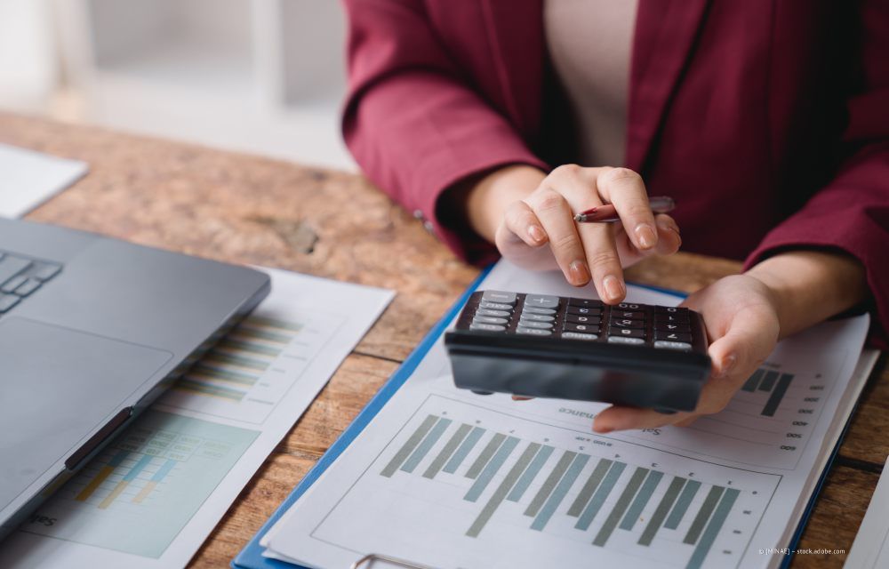 Wohnzimmer mit olivgrünem Sofa, Holztischen, Topfpflanze und Stehlampe.