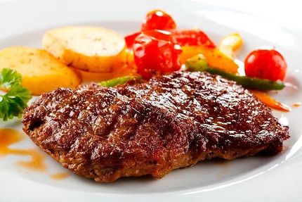 Bistec con patatas y verduras en un plato blanco.