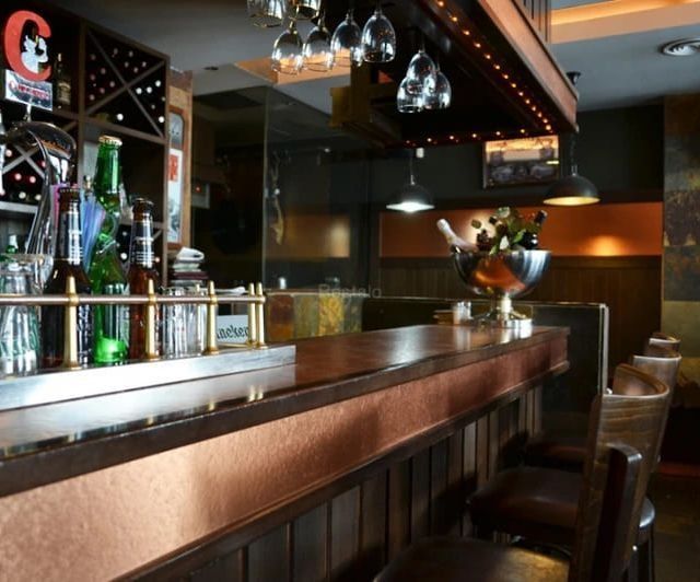 Interior de un bar con detalles de madera, molduras de cobre y botellas expuestas.