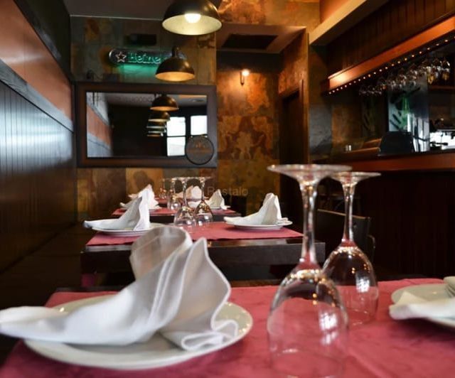 Área de comedor del restaurante con mesas preparadas, copas de vino y una barra visible al fondo.