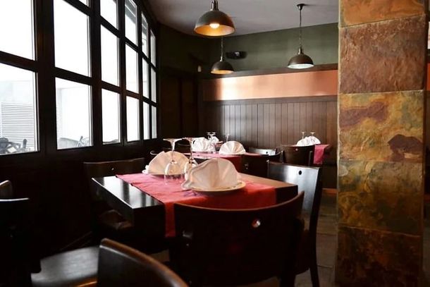 Interior de restaurante con mesas preparadas para el servicio, madera oscura y detalles de piedra.