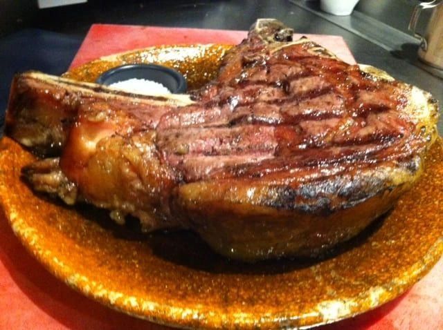 Filete de costilla con hueso a la parrilla en un plato marrón con un pequeño plato de sal.