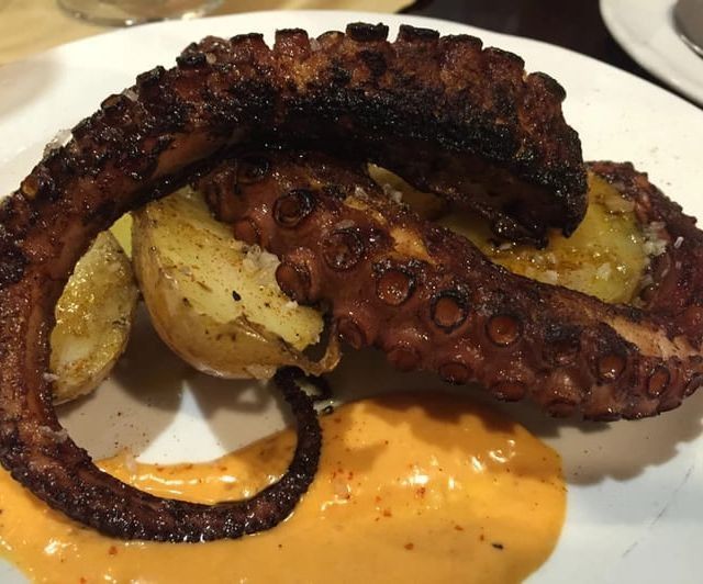 Pulpo a la plancha con patatas y salsa de naranja en plato blanco.