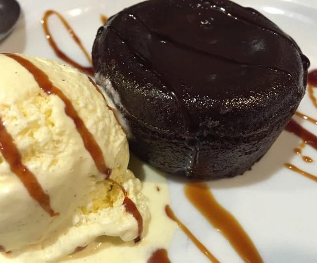 Pastel de lava de chocolate con helado de vainilla, rociado con caramelo en un plato blanco.