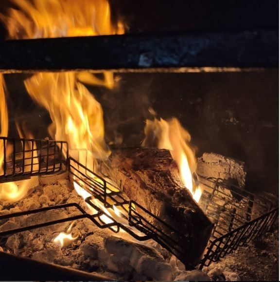 Llamas ardiendo en una chimenea, leña en la parrilla, con brasas brillantes y un interior oscuro.