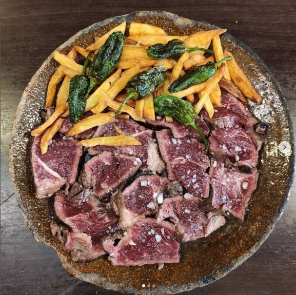 Rebanadas de filete sellado, papas fritas y pimientos verdes fritos en un plato rústico.