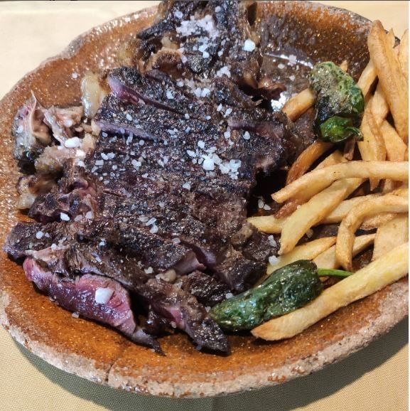 Bistec a la parrilla con patatas fritas y pimientos en un plato marrón.